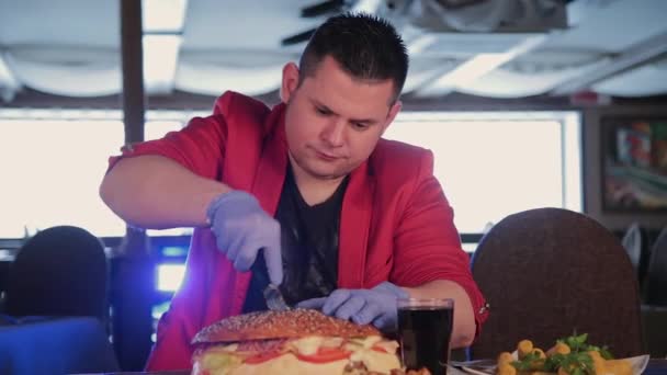 A man cuts a huge burger with a knife. — Stock Video