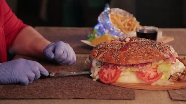 Un uomo taglia un hamburger enorme con un coltello . — Video Stock