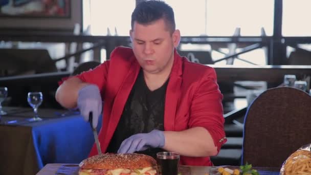 Un uomo taglia un hamburger enorme con un coltello . — Video Stock