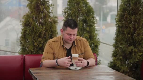 Człowiek pije latte na werandzie przy stole. — Wideo stockowe