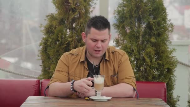 L'homme buvant du latte sur la véranda à la table . — Video