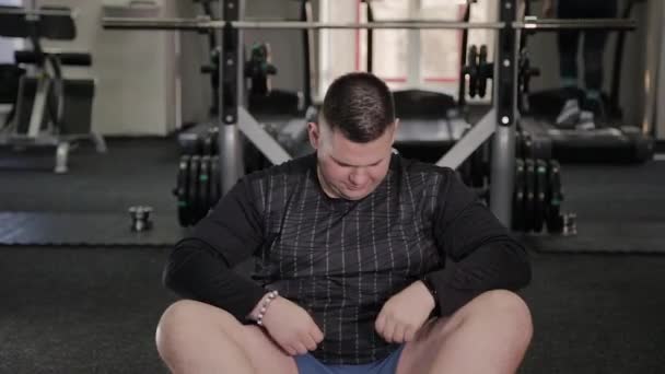 Tlustý muž dělá strečink na podlahu v tělocvičně. — Stock video