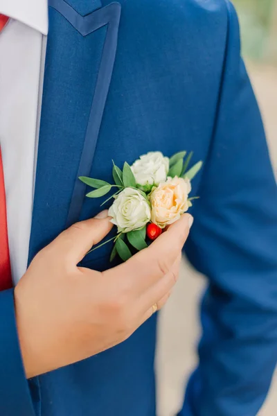 Lo sposo raddrizza il boutonniere di fiori sulla giacca . — Foto Stock