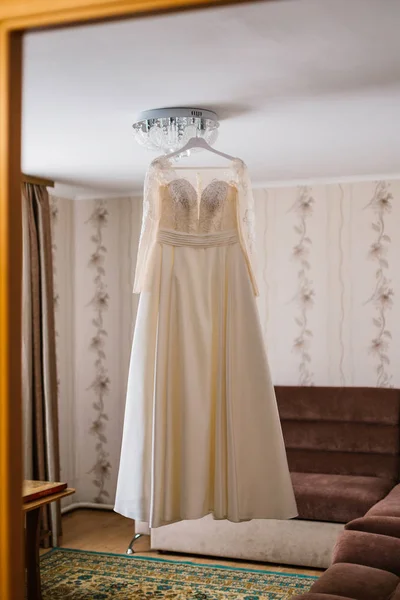 Vestido de novia muy hermoso de la novia colgando en la lámpara de araña en la habitación . —  Fotos de Stock