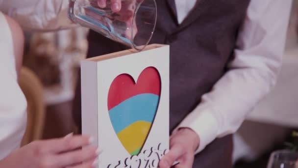 Ceremonia de arena en la boda. El novio cierra el tubo de vaso de vidrio lleno de arena de diferentes colores en el banquete de bodas en el interior . — Vídeos de Stock