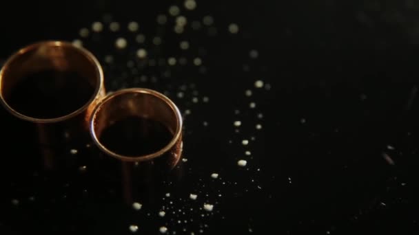 Wedding rings lying on dark surface with reflection and water. Shining with light close up macro. — Stock Video