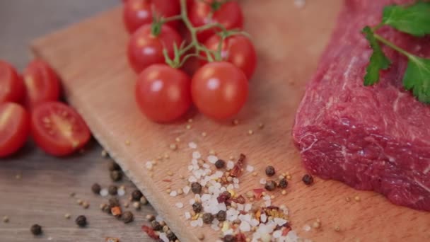 Syrové hovězí maso na dřevěné pozadí s kořením a rajčaty. — Stock video