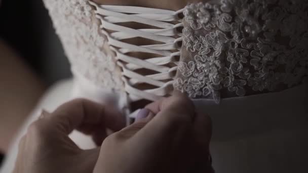 Close up of back of young bride getting ready for wedding ceremony. Mother helping her daughter to dress up bridal dress. Close up of lace and aged female hands. Real time full hd video footage — Stock Video