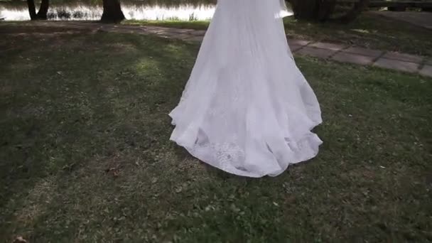 Beautiful young bride walks on the grass with a train of wedding dress. — Stock Video