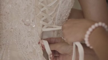 Bir genç gelin düğün töreni için hazırlanıyor arka kapatın. Anne kızı gelin giysi elbise yardım. Dantel ve yaşlı kadın elleri yakın. Gerçek zamanlı tam hd video görüntüleri