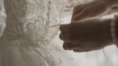 Bir genç gelin düğün töreni için hazırlanıyor arka kapatın. Anne kızı gelin giysi elbise yardım. Dantel ve yaşlı kadın elleri yakın. Gerçek zamanlı tam hd video görüntüleri