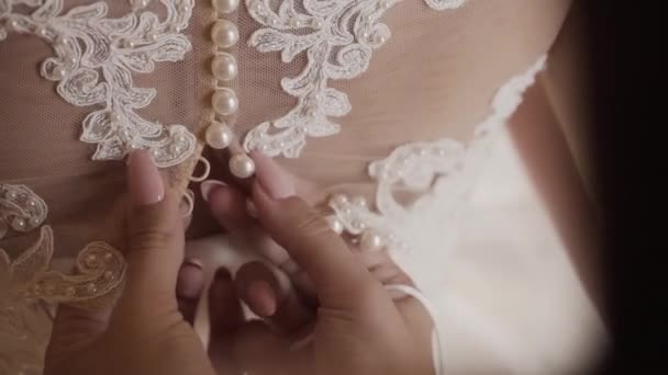 Close-up de volta da jovem noiva se preparando para a cerimônia de casamento. Mãe ajudando sua filha a vestir-se vestido de noiva. Feche de rendas e mãos femininas envelhecidas. Tempo real full hd vídeo footage — Vídeo de Stock