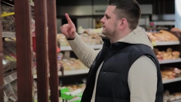 Fat Man in de supermarkt kiest voor snoepjes voor zichzelf. — Stockvideo