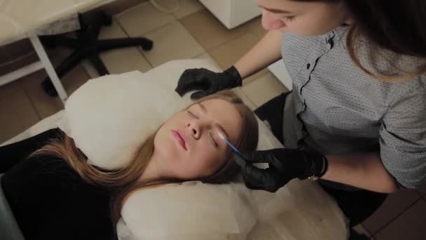 Ein sehr schönes Mädchen in einem Schönheitssalon macht eine Laminierung Wimpern. Kosmetikerin führt den Eingriff Wimpernfragmentierung durch. — Stockvideo