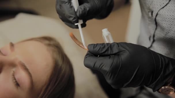 Una chica muy hermosa en un salón de belleza hace una laminación pestañas. esteticista aplica pegamento a las pestañas . — Vídeo de stock