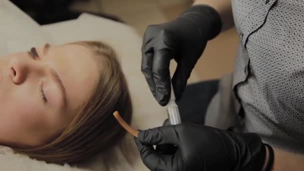 Una chica muy hermosa en un salón de belleza hace una laminación pestañas. esteticista aplica pegamento a las pestañas . — Vídeos de Stock