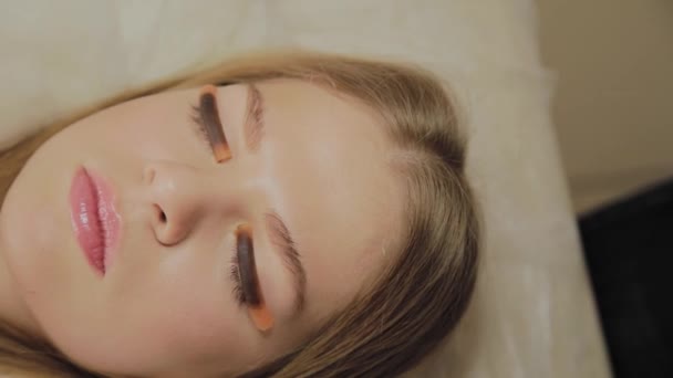 Een zeer mooi meisje in een schoonheidssalon heeft een lamineren wimpers. Wachten op lijm op wimpers te drogen — Stockvideo