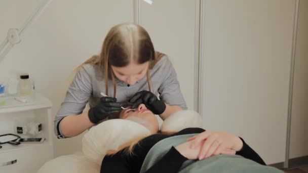 Ein sehr schönes Mädchen in einem Schönheitssalon macht eine Laminierung Wimpern. Kosmetikerin führt den Eingriff Wimpernfragmentierung durch. — Stockvideo