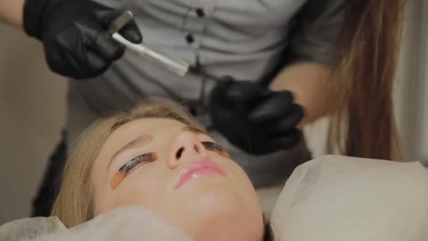 Une très belle fille dans un salon de beauté fait une plastification des cils. Esthéticienne effectue la procédure de fragmentation des cils . — Video
