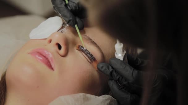 Ein sehr schönes Mädchen in einem Schönheitssalon macht eine Laminierung Wimpern. Kosmetikerin führt den Eingriff Wimpernfragmentierung durch. — Stockvideo