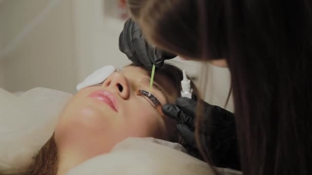 Une très belle fille dans un salon de beauté fait une plastification des cils. Esthéticienne effectue la procédure de fragmentation des cils . — Video