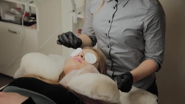 Une très belle fille dans un salon de beauté fait une plastification des cils. Esthéticienne effectue la procédure de fragmentation des cils . — Video