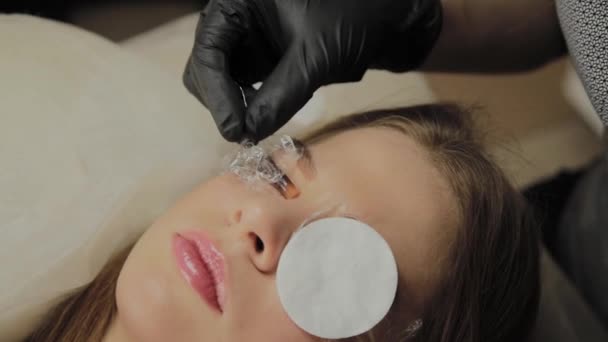 Une très belle fille dans un salon de beauté fait une plastification des cils. Esthéticienne effectue la procédure de fragmentation des cils . — Video