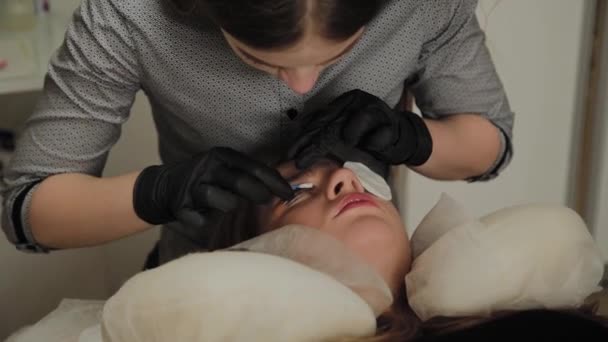 Ein sehr schönes Mädchen in einem Schönheitssalon macht eine Laminierung Wimpern. Kosmetikerin führt den Eingriff Wimpernfragmentierung durch. — Stockvideo