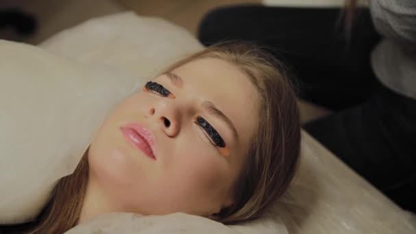 Ein sehr schönes Mädchen in einem Schönheitssalon macht eine Laminierung Wimpern. auf trockener Farbe auf den Wimpern wartend. — Stockvideo