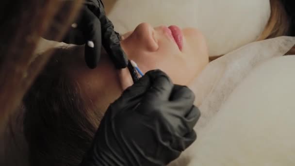 Une très belle fille dans un salon de beauté fait une plastification des cils. Esthéticienne effectue la procédure de fragmentation des cils . — Video