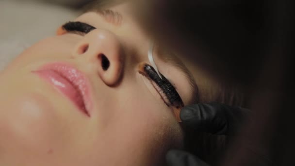 Ein sehr schönes Mädchen in einem Schönheitssalon macht eine Laminierung Wimpern. Kosmetikerin führt den Eingriff Wimpernfragmentierung durch. — Stockvideo