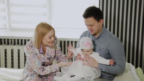 Familia feliz jugando con su hija pequeña en una cama blanca . — Vídeo de stock