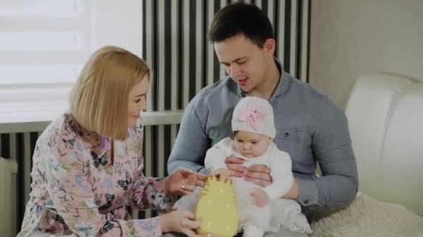 Familia feliz jugando con su hija pequeña en una cama blanca . — Vídeo de stock