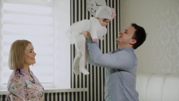 Familia feliz jugando con su hija pequeña en una cama blanca . — Vídeos de Stock