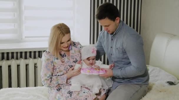 Familia feliz jugando con su hija pequeña en una cama blanca . — Vídeo de stock