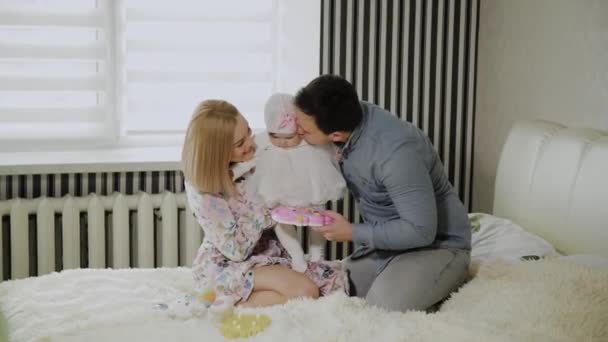 Щаслива сім'я грає зі своєю маленькою донькою на білому ліжку . — стокове відео