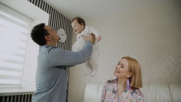 Familia feliz jugando con su hija pequeña en una cama blanca . — Vídeos de Stock