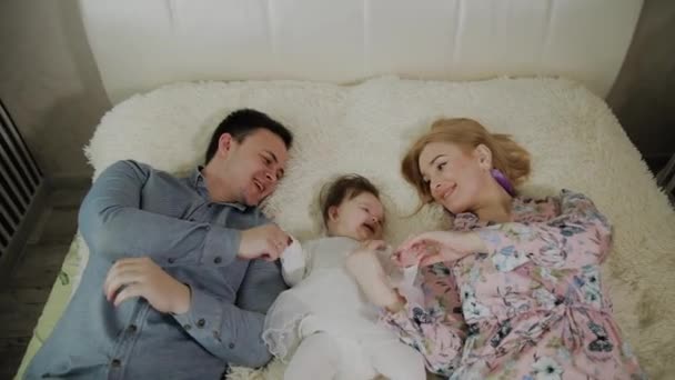 Anyák napja. Fiatal aranyos vidám család hugginh az ágyban. Anya, apa és a kis aranyos lánya közepén — Stock videók