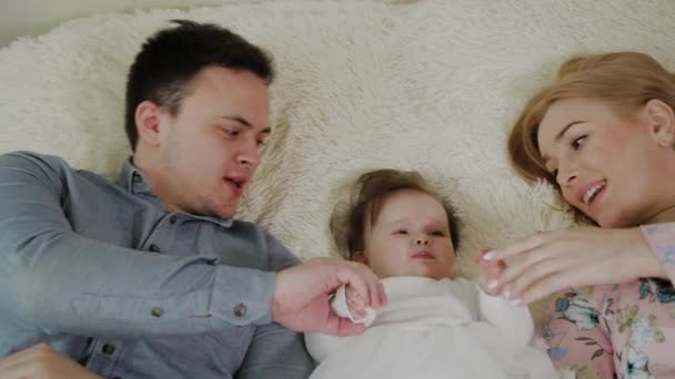 Mothers day. Young cute cheerful family is hugginh in the bed. Mom, dad and little cute daughter in the middle — Stock Video