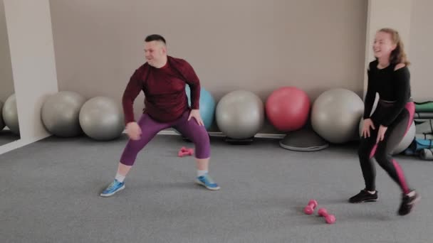 Pozitivní obézní žena a fit chlap dělá cvičení zatímco sedí na podlaze. zábavné učení — Stock video