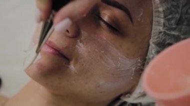 Kapalı spa salonda yalancı kadının yüzünde maske yetenekli güzellik uzmanı koyar.
