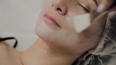 Kapalı spa salonda yalancı kadının yüzünde maske yetenekli güzellik uzmanı koyar.