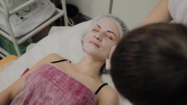 Kapalı spa salonda yalancı kadının yüzünde maske yetenekli güzellik uzmanı koyar.