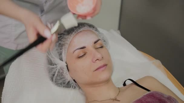 Il cosmetologo esperto mette la maschera su faccia di donna trovante in salone di centro termale all'interno . — Video Stock