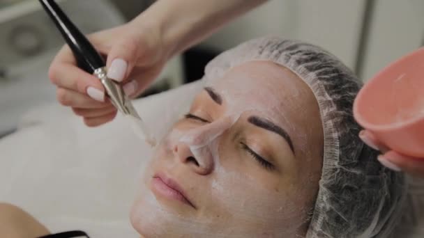 Skilled cosmetologist puts mask on face of lying woman in spa salon indoors. — Stock Video