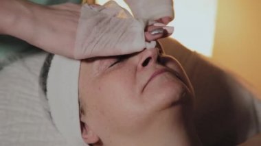 Profesyonel bir güzellik prosedürü için yaşlı bir kadının yüzünü hazırlar. Kozkolojik yenilikler