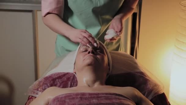 Профессиональный косметолог готовит лицо пожилой женщины к процедуре. Косметологические инновации — стоковое видео