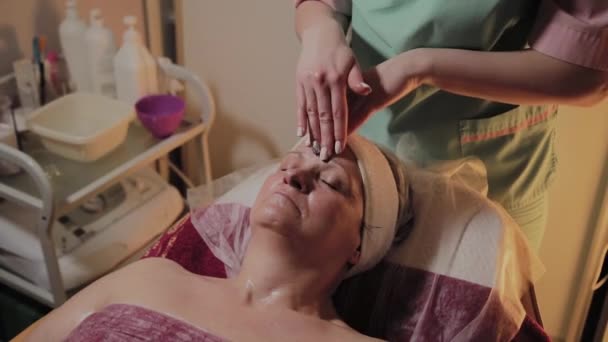 Cosmetologist profissional faz a massagem a uma mulher idosa. Inovações cosmológicas — Vídeo de Stock
