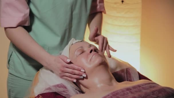 Профессиональный косметолог делает массаж пожилой женщине. Косметологические инновации — стоковое видео