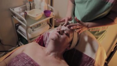 Profesyonel Kozmetolog yaşlı bir kadına masaj yapar. Kozkolojik yenilikler